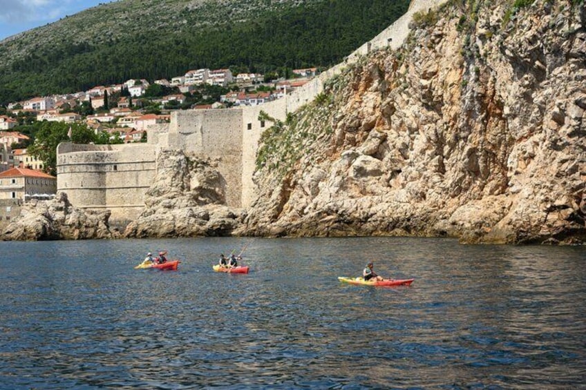 Three kayaks on calm water near a rocky coastline with houses in the background. 2