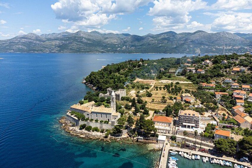 A coastal town with a prominent church, clear blue sea, and mountainous backdrop. 1
