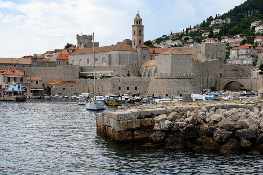 A historic waterfront with stone buildings, a prominent tower, and boats docked at the pier. 5