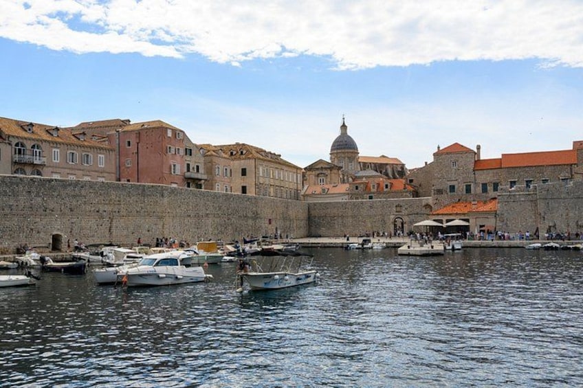 A harbor with boats, a stone wall, and historic buildings with domed architecture. 4
