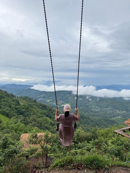A person on a swing overlooking a mountainous landscape. 2