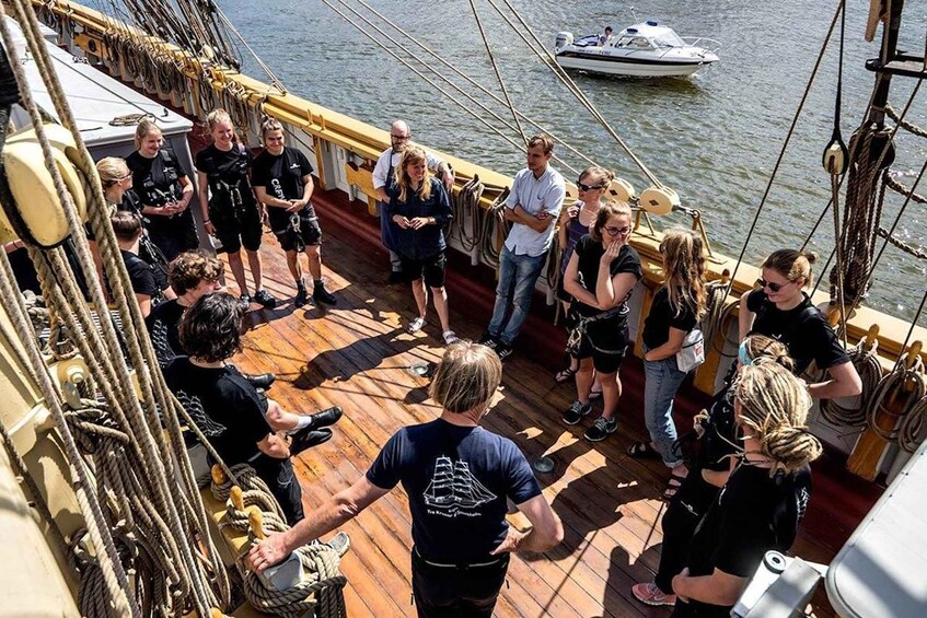A group of people on a wooden deck of a ship, with ropes and rigging visible. 3