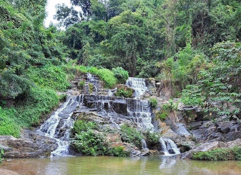 A multi-tiered waterfall cascading over rocks into a calm pool surrounded by dense greenery. 1