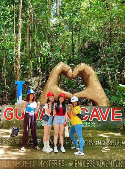 A group of people posing in front of a cave entrance with a heart-shaped structure and a sign that reads 'GUYNE CAVE.' 3