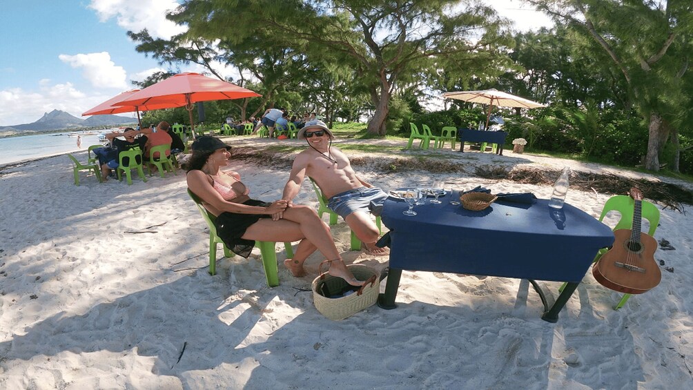 A couple sitting at a table on a sandy beach with a guitar and a bottle of wine. 3