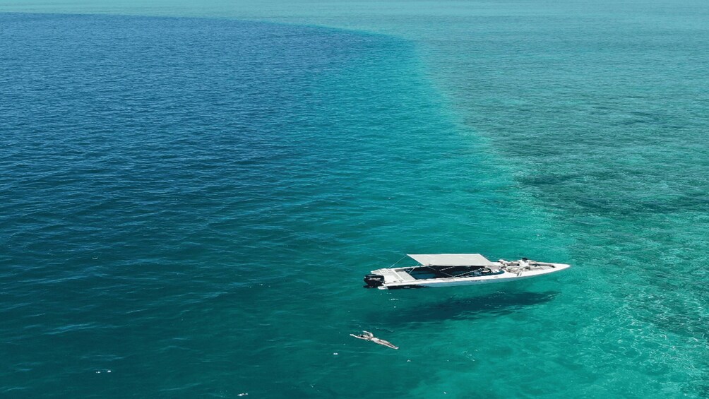 A boat on clear turquoise water with a person swimming nearby. 1