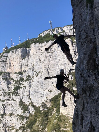 Two individuals rock climbing on a cliff with white rock faces and sparse vegetation. 3