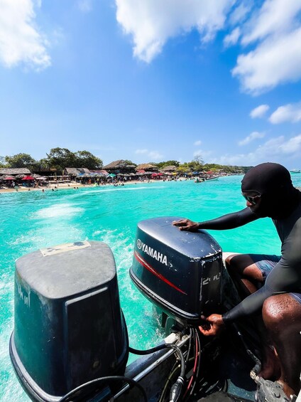 A person on a boat with a Yamaha outboard motor, a turquoise sea, and a beach with umbrellas and people in the background. 3