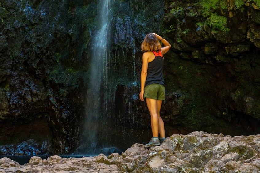 A person standing on rocks, looking at a waterfall. 2