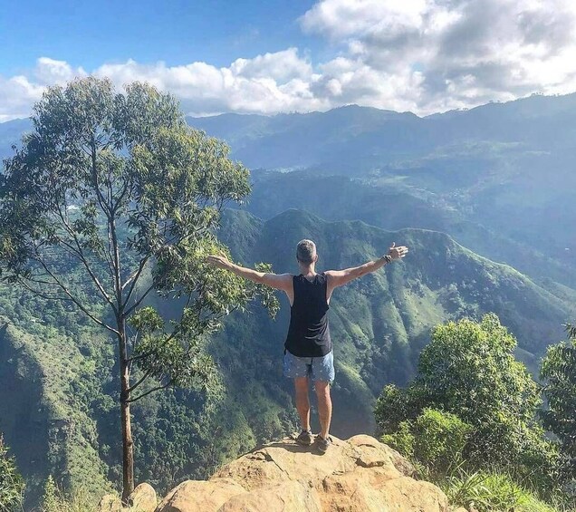 A person standing on a rock with arms outstretched, overlooking a mountainous landscape. 5