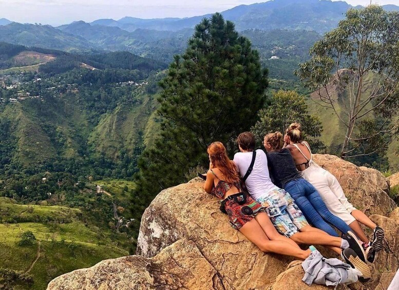 A group of people sitting on a rock overlooking a mountainous landscape. 4