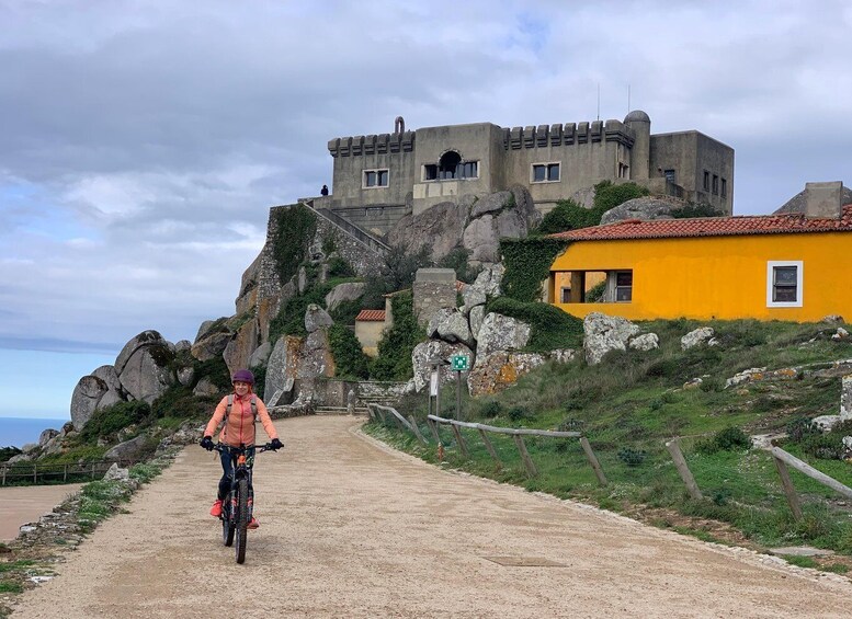 A cyclist on a dirt path leading to a castle-like structure with a yellow building nearby. 4