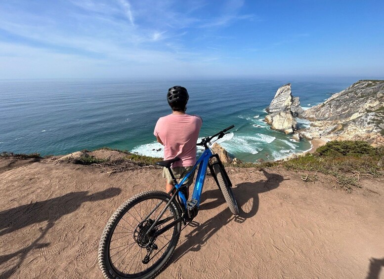 A person sitting on a mountain bike overlooking a coastal cliff and ocean. 1
