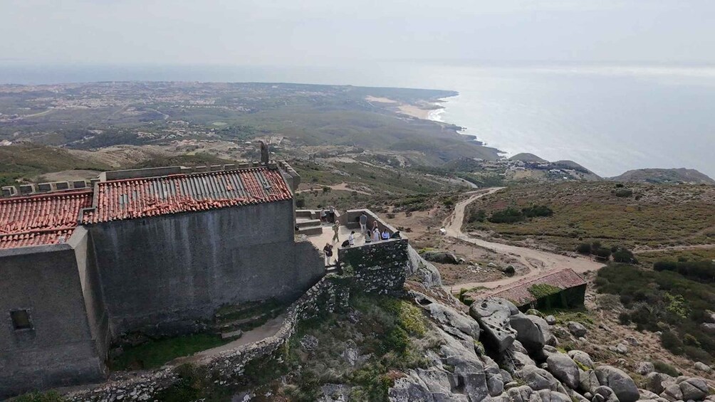 A coastal fortification with a red-tiled roof overlooking a winding road and the ocean. 3