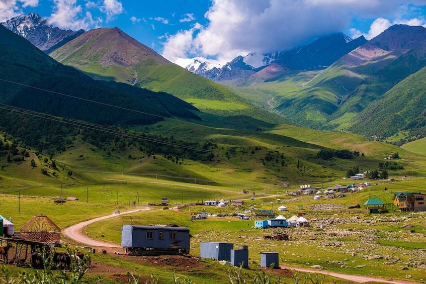 A rural village with houses, a dirt road, and mountains in the background. 2