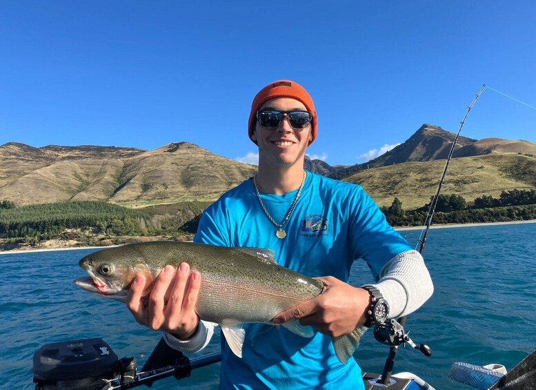 A person holding a fish on a boat with a mountainous landscape in the background. 2