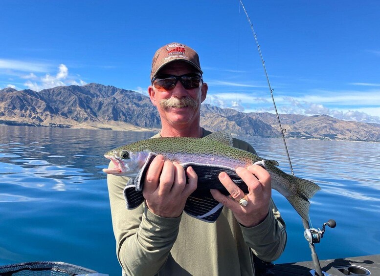 A person holding a fish with a mountainous landscape in the background. 1