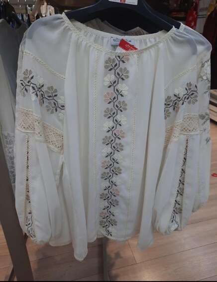 A white blouse with floral embroidery and lace details on a hanger. 2