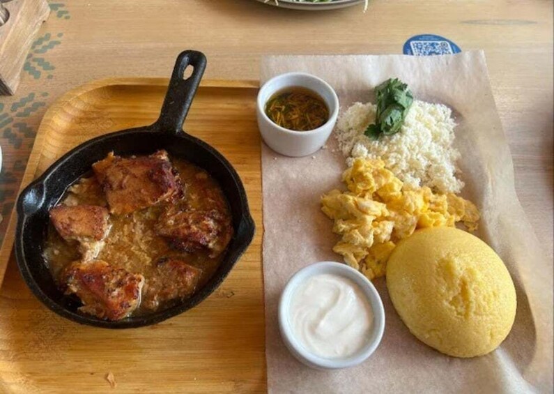 A skillet with meat, scrambled eggs, rice, and a yellow bread on a wooden board. 5