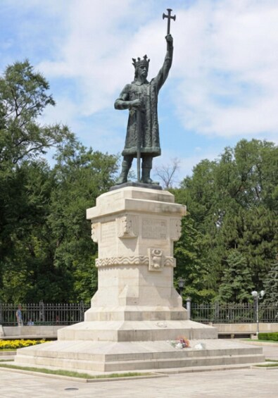 A statue of a figure holding a cross on a pedestal in a park. 3