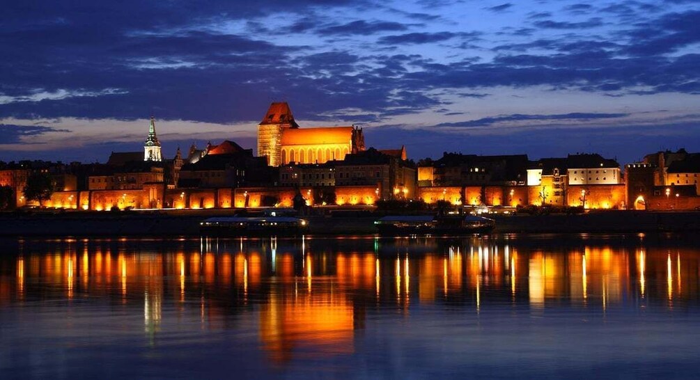 A historic cityscape at dusk with illuminated buildings reflecting on the water. 1