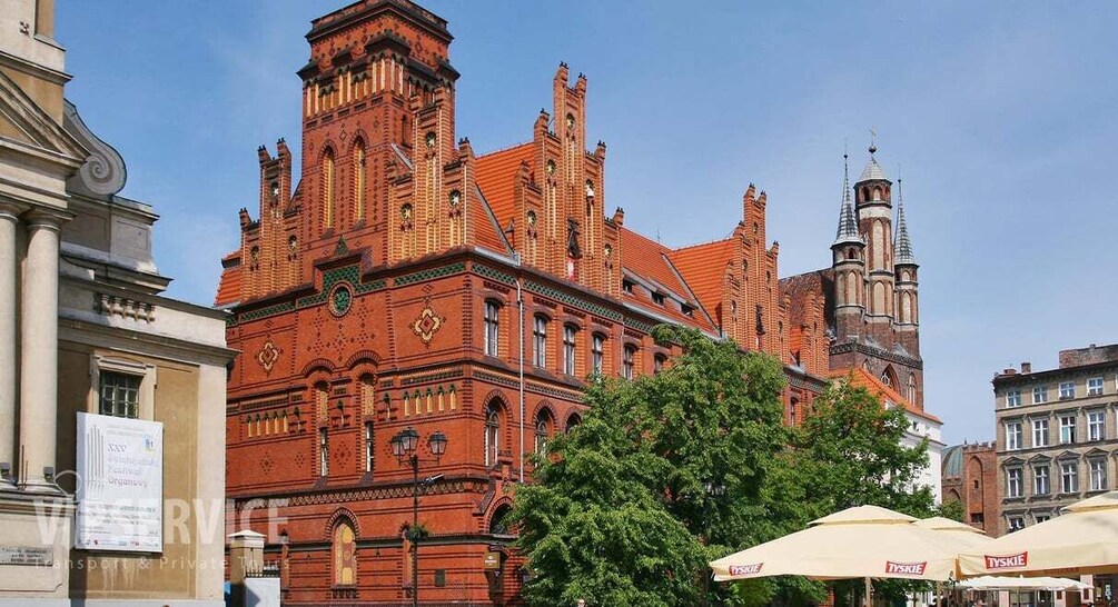 A historic red brick building with ornate architecture, a clock tower, and a clear blue sky. 3