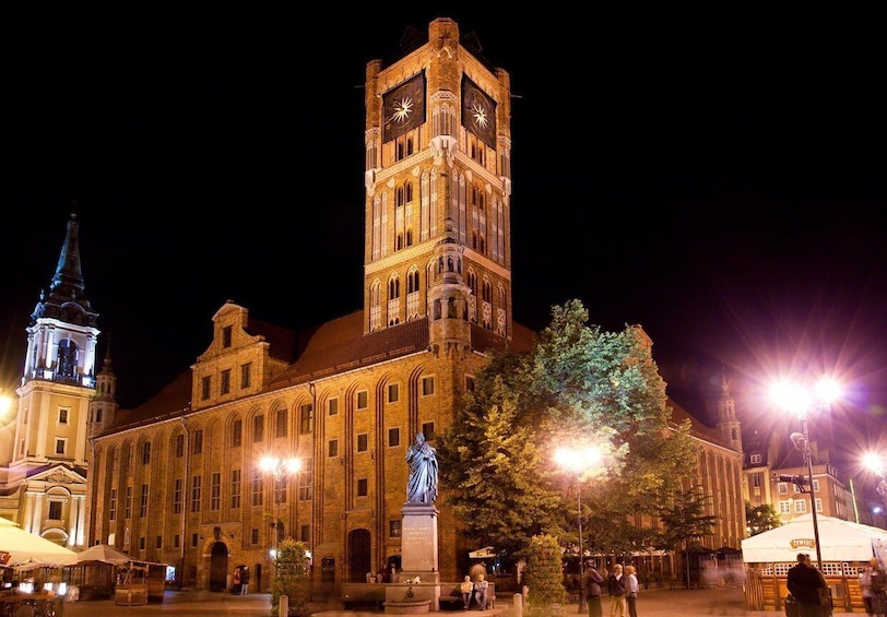 A historic building with a clock tower, a statue in front, and a market area with tents. 2