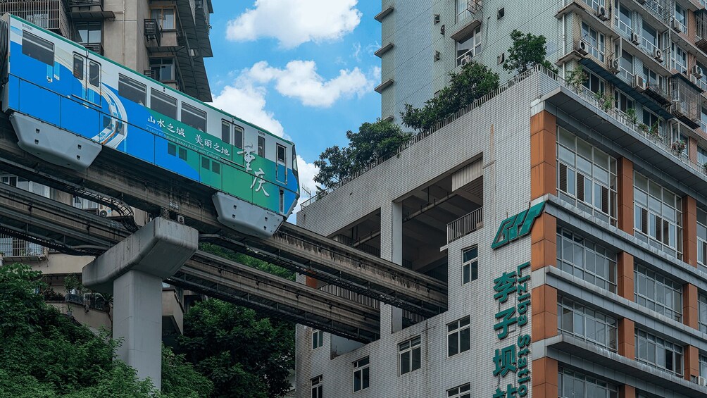 A train on an elevated track passing by a modern building with foreign signage. 2