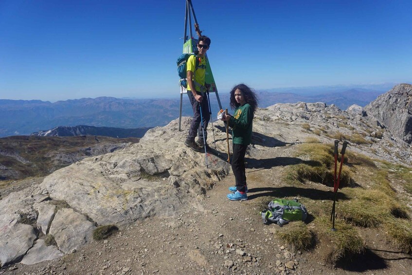 Two people standing on a rocky mountain peak with a clear sky. 3