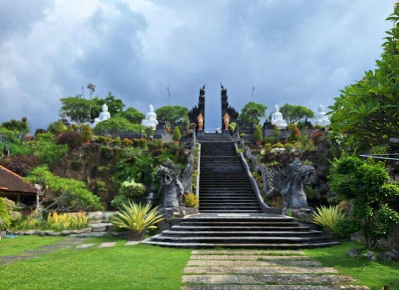 A temple complex with a central staircase leading to a roofed structure, surrounded by lush greenery and statues. 2