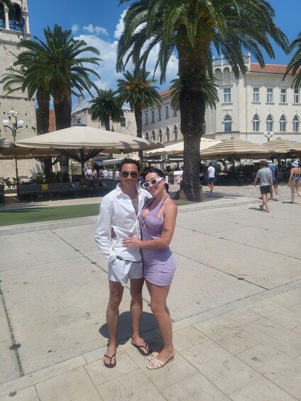 A couple posing in a public square with palm trees and historic buildings in the background. 3