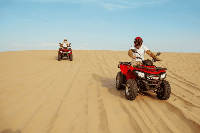 Two people riding red ATVs on a sandy dune. 1