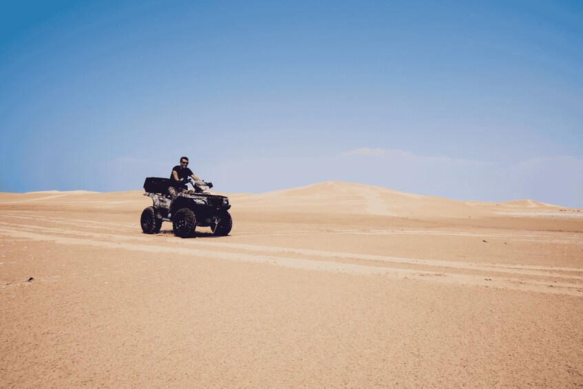 A person on a quad bike in a desert with sand dunes. 3