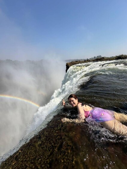 A person lying on rocks near a waterfall with a rainbow. 2