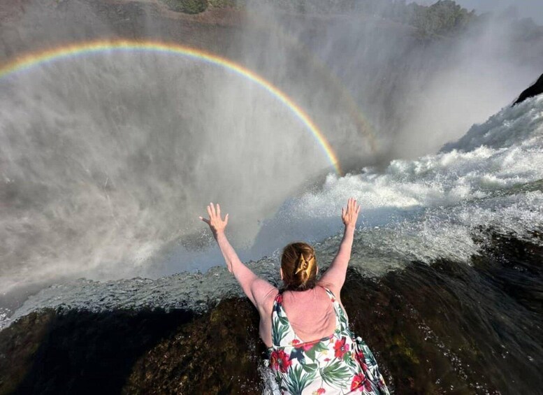 A person standing with arms raised, facing a waterfall with a rainbow. 1
