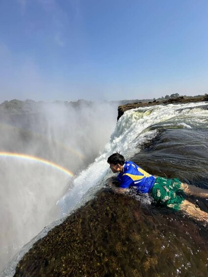 A person lying on a rock by a waterfall with a rainbow. 3