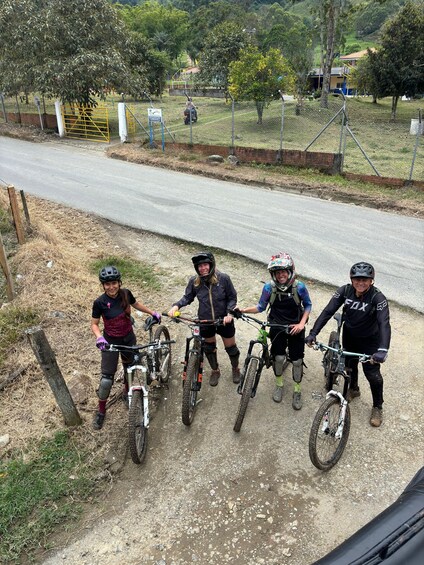 Four mountain bikers on a dirt trail with a road in the background. 4