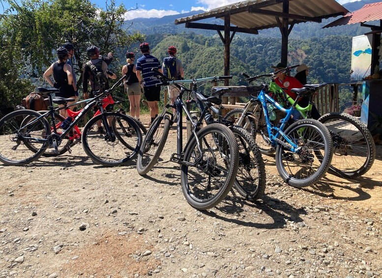 A group of cyclists at a mountain biking trailhead with various bikes parked and a scenic view of the mountains in the background. 5