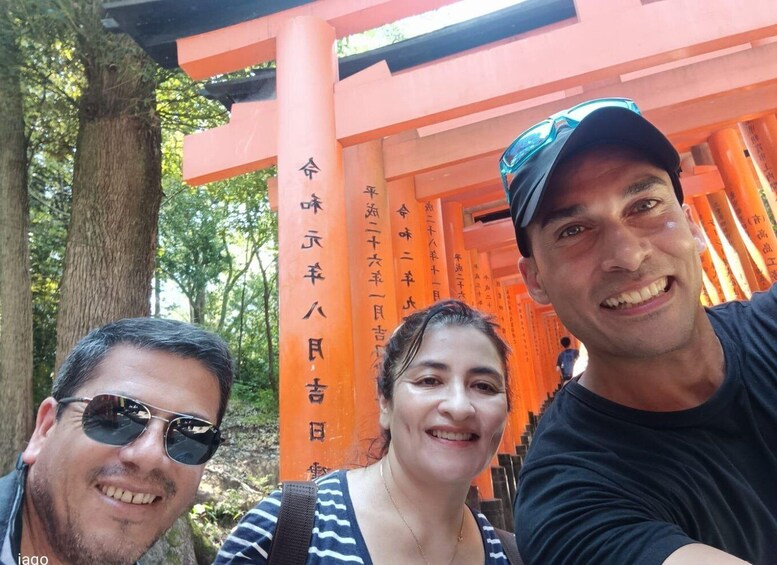 Three people in front of orange torii gates with Japanese inscriptions. 4