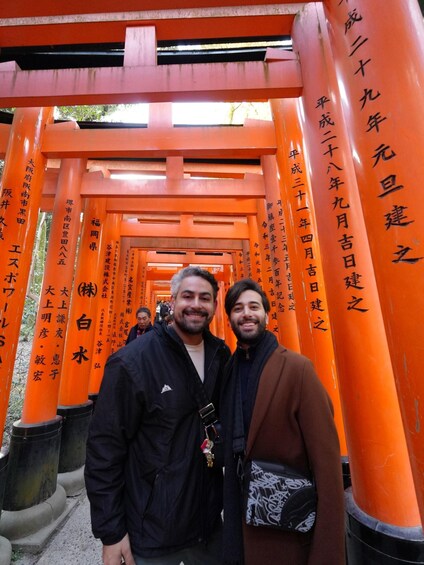 Two people standing in front of a row of orange torii gates with Japanese inscriptions. 3
