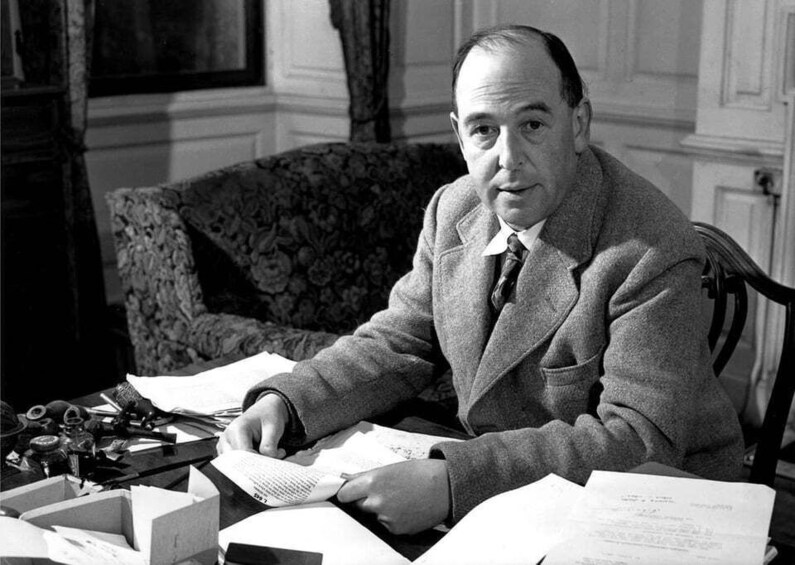 A man in a suit sitting at a desk with papers and a typewriter. 1