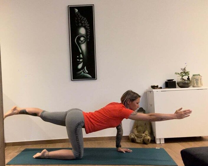 A person performing a yoga pose on a mat in a room with a Buddha painting and a statue. 5