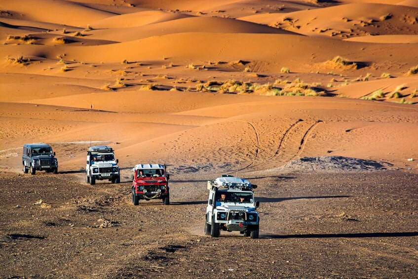 Four off-road vehicles on a desert terrain with sand dunes. 1