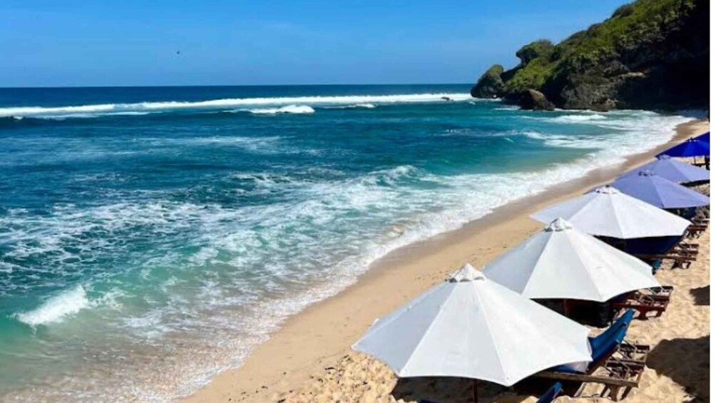 A beach with waves, umbrellas, and chairs. 4