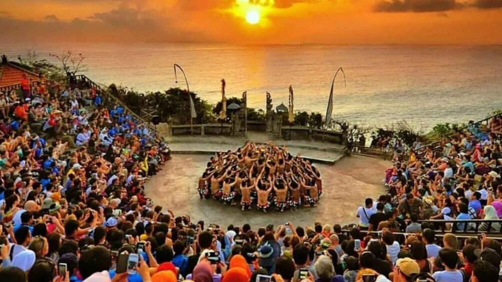 A sunset over the ocean with a crowd watching a performance on a stage. 5