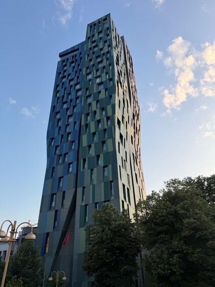 A tall, modern building with a geometric facade, surrounded by trees and a clear sky. 2