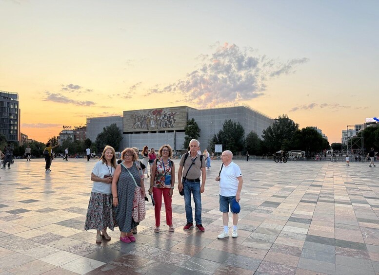 A group of people standing in a plaza with a large mural and a building in the background. 5