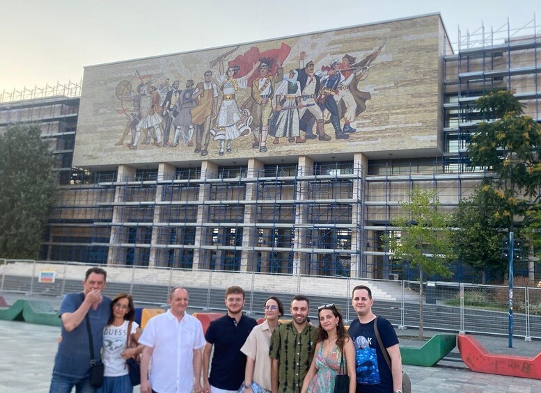 A group of people in front of a building with a large mural depicting historical figures. 1