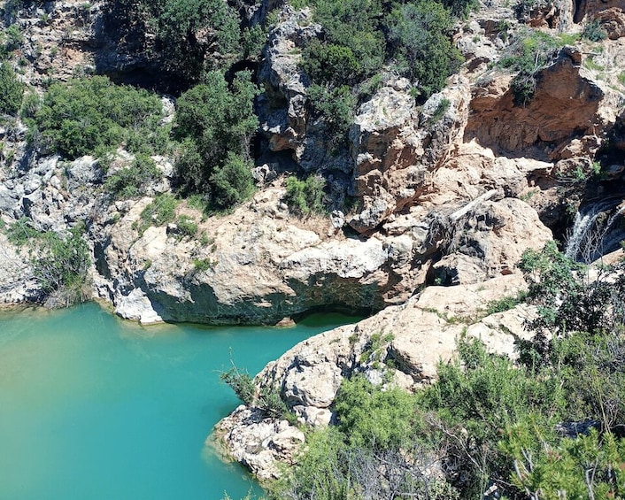 A rocky landscape with a turquoise pool surrounded by cliffs and sparse vegetation. 2