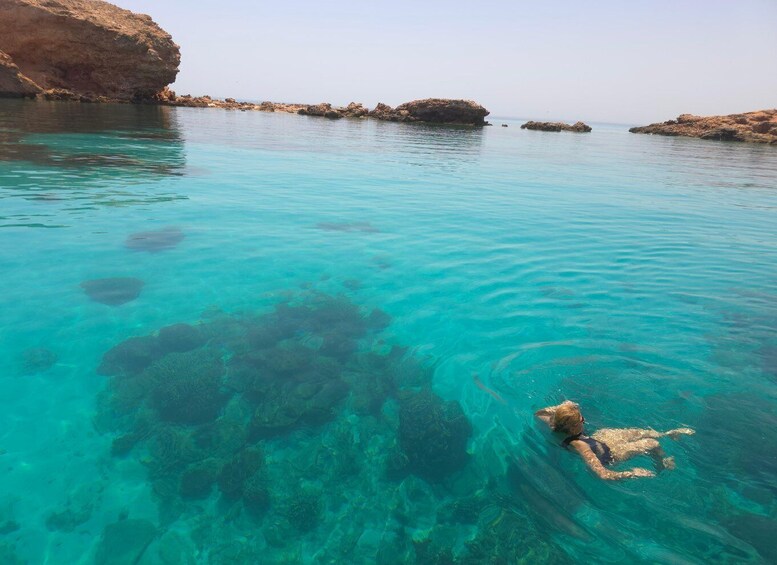 A swimmer in clear turquoise water near rocky formations. 3